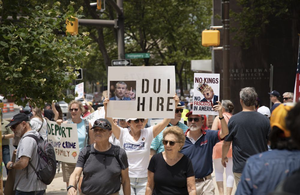 Person in crowd holding sign with picture of Pete Hegseth and saying 