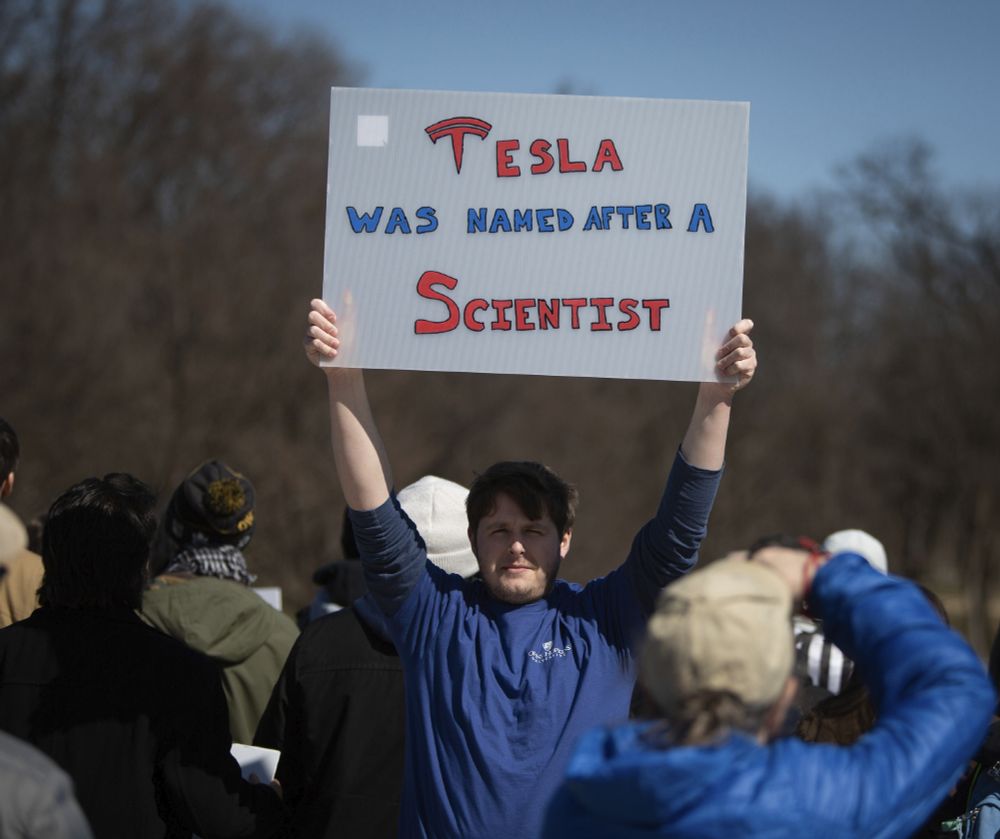 Person holding a TESLA WAS NAMED AFTER A SCIENTIST sign.