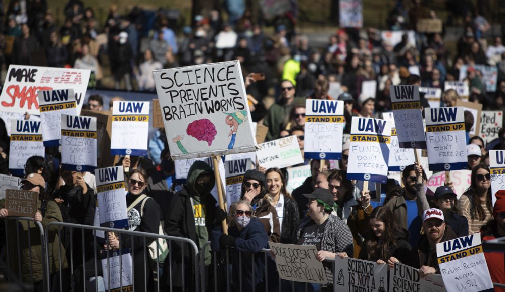 A large crowd in front of the speaker's platform, focused on a sign that says SCIENCE PREVENTS BRAIN WORMS.