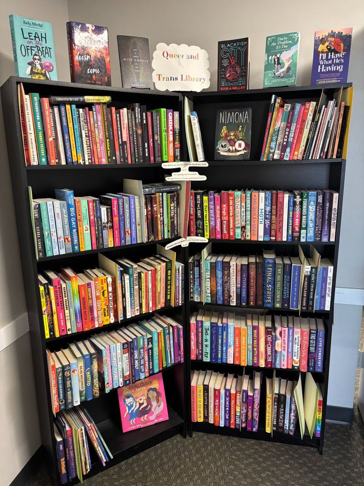 A picture of a black bookshelf labeled 'Queer and Trans Library'