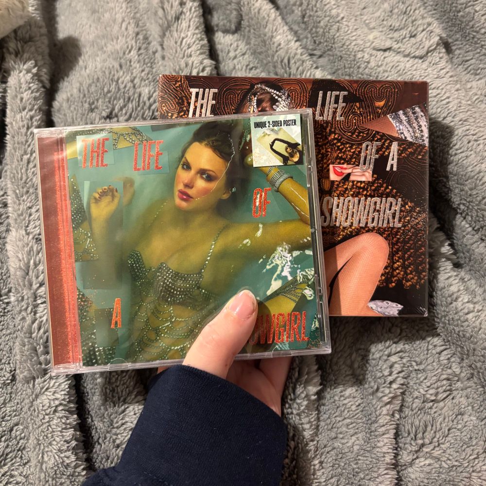 a photo of two Taylor Swift, the life of a showgirl albums in front of a grey blanket.