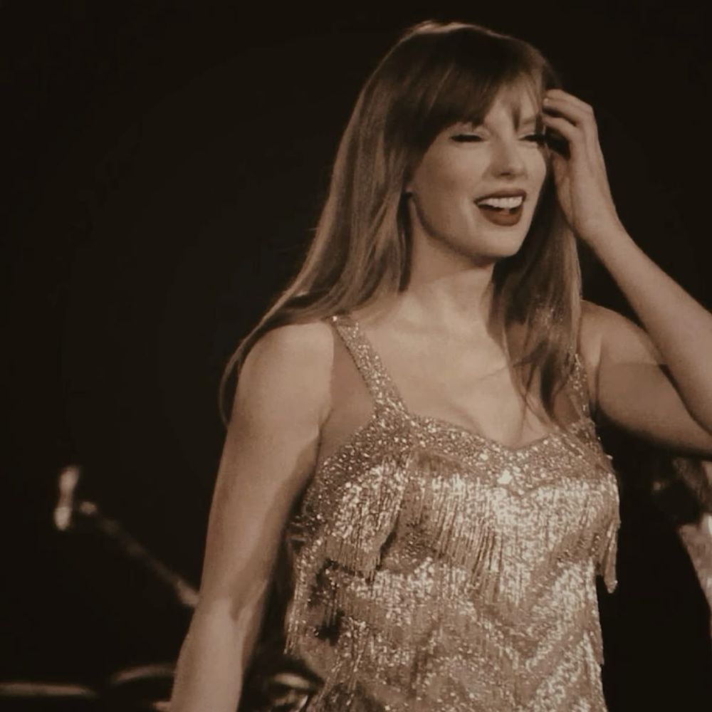 Taylor Swift with a golden filter, with a sparkly dress and smiling with her hand in the hair