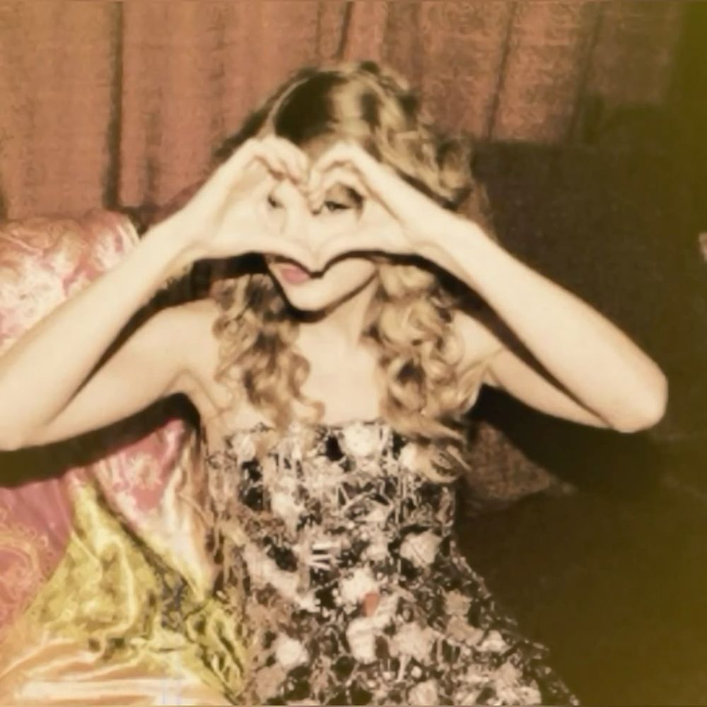 Taylor Swift in the OG Fearless era doing a hand heart in front of her face.