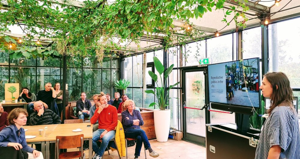 People sitting at tables listening to a presentation in a green house