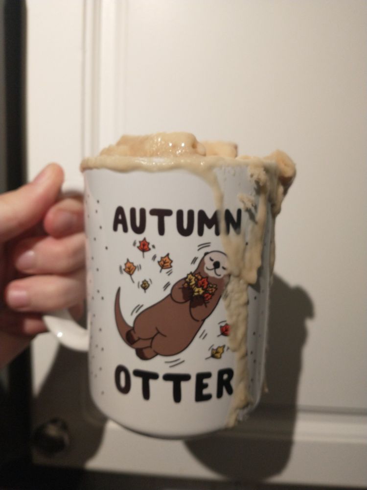 A mug that says "Autumn Otter" and has a picture of an otter with colorful leaves. The mug is overflowing with batter