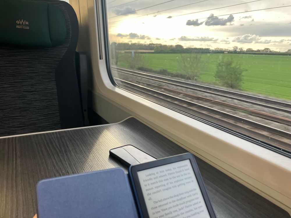  View from a train window, with Kindle device open on the table. View through the window shows a sunset over the countryside.