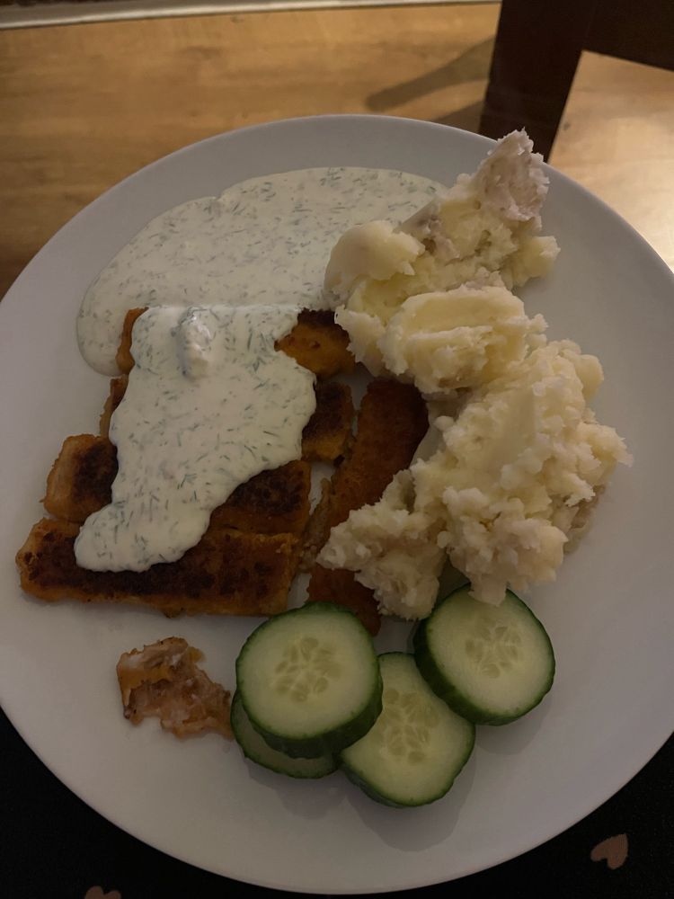 Bild på fem fiskpinnar nästan helt täckta i vit dillsås, potatismos och gurkskivor