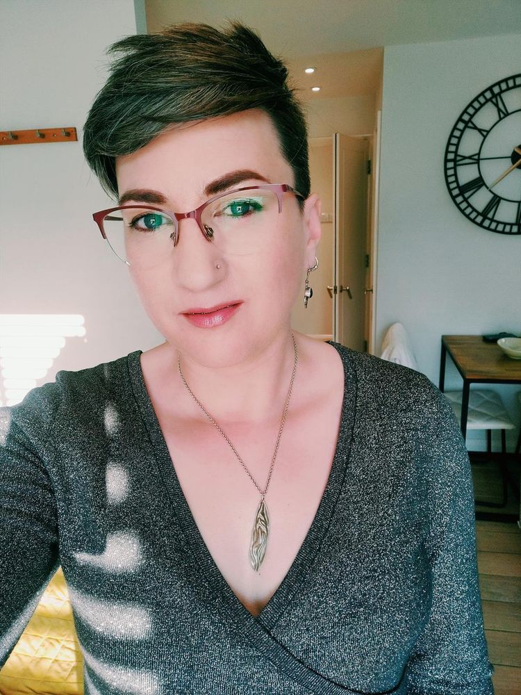 Selfie of me, a white femme with short brown hair and glasses, wearing a low cut sparkly silver dress and looking pretty damn sultry if I do say so myself