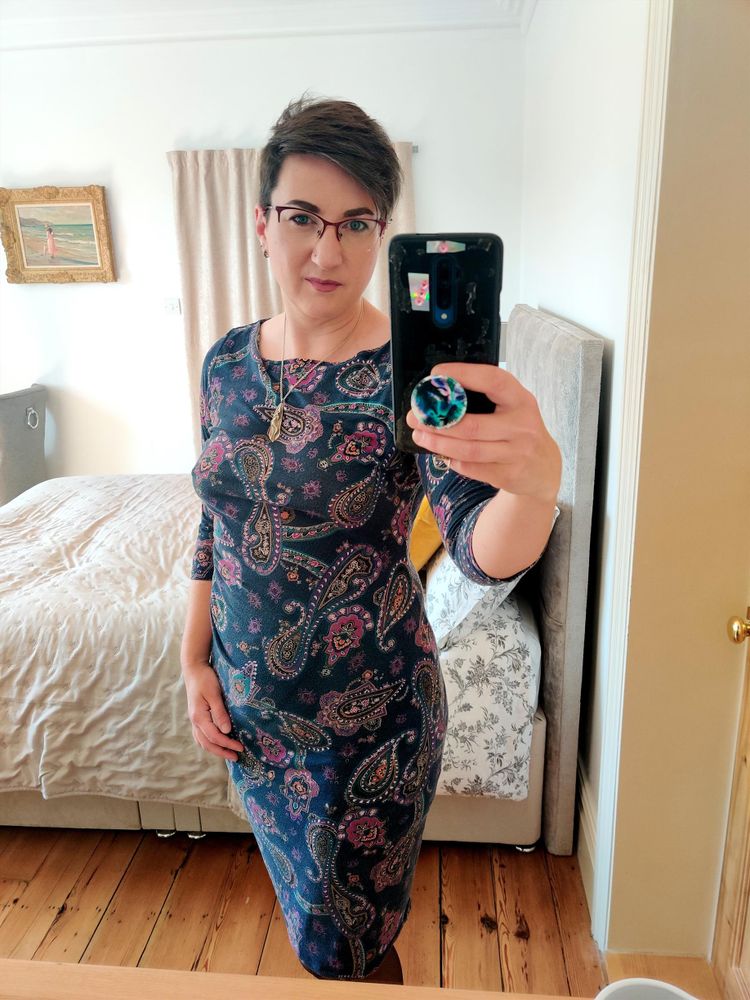 Selfie of me, a non-binary femme with short brown hair and glasses, wearing a figure-hugging dress and showing off my curves in a bedroom mirror