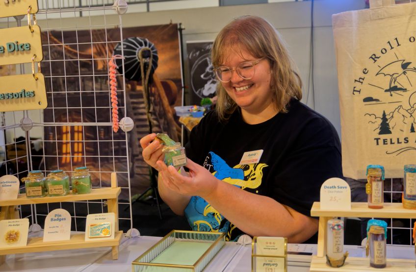 A photo of a smiling woman with a black shirt demonstrating one of her products, a gelatinous cube in a jar.