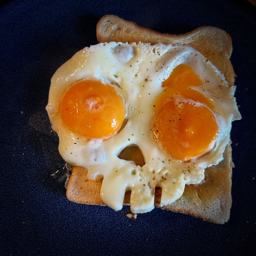A fried egg on toast, sat on a blue plat. However, the egg is in the shape of a skull with yolks for each of its eyes.