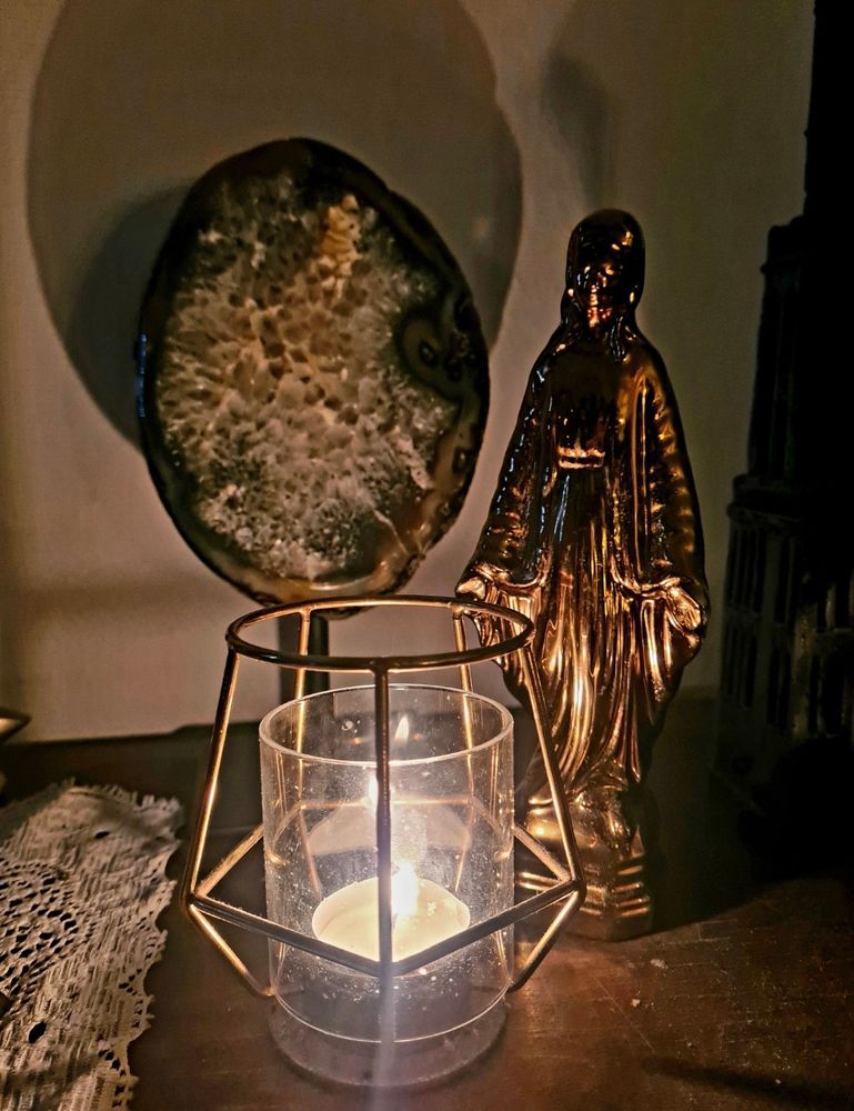 Een brandend waxinelichtje, omgeven door een randje van de Utrechtse Dom, een gouden Maria-beeldje en een Agaath. Ook is een stukje van een wit gehaakt kleedje zichtbaar. 