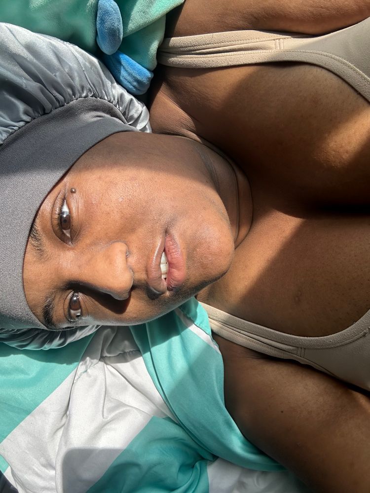 A woman laying in bed underneath the sun in a sliver bonnet