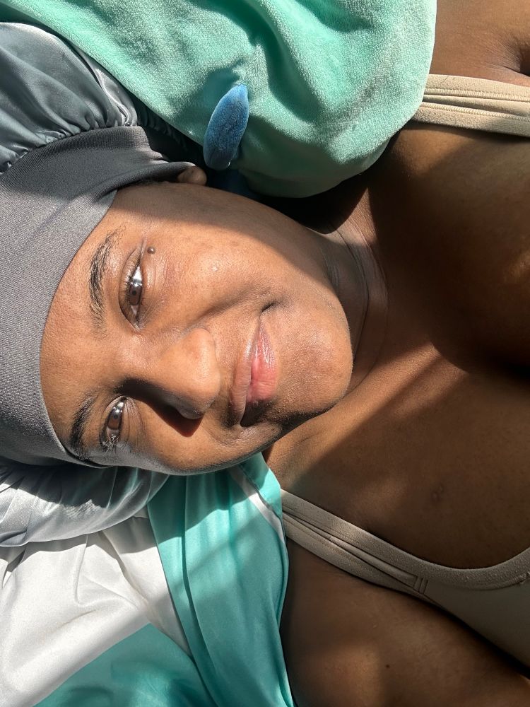 A woman laying in bed underneath the sun in a sliver bonnet smiling