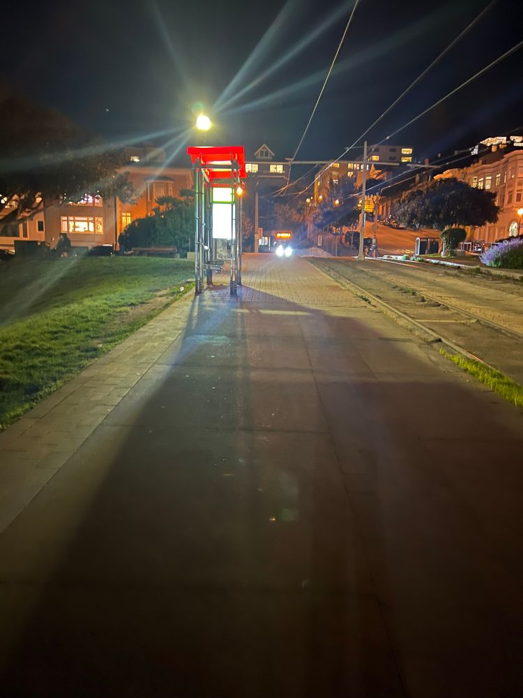 Nighttime view of the 20th St stop (top of the hill at Dolores Park) with an eastbound J approaching.