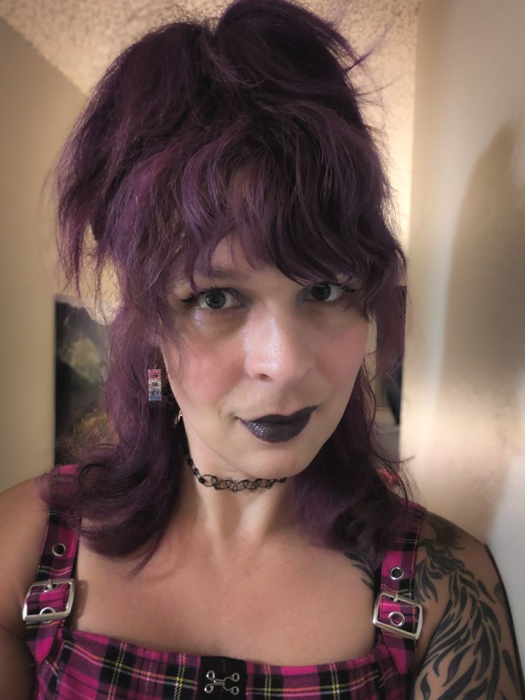 Zoe in black lipstick and big purple hair, and a very 90s pink top. 