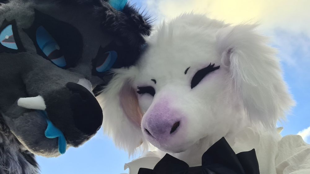 White dog fursuit and grey deer with blue eyes pose towards the camera 