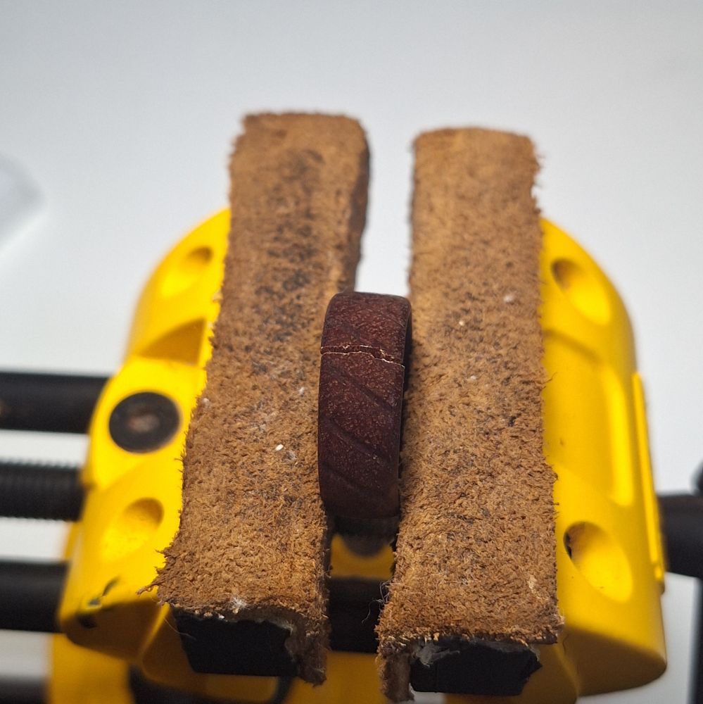 A wooden ring held in a bench vice. It has a crack running along splitting it in twain.