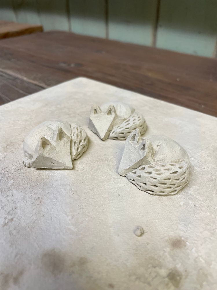 Three clay foxes, they’re curled up and appear to be sleeping. 