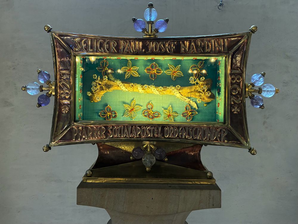 eine reliquie in einem goldenen rahmen:
großer oberschenkelknochen in goldband gewickelt, der rahmen ist verziert mit perlenstickereien.