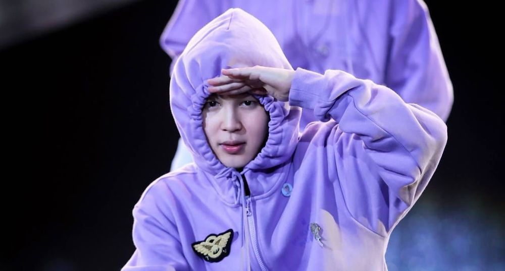 Jimin wearing a light purple hoodie with the hood so tight that we can only see his face, not his hair! He has his left hand over his eyes, as is he is scanning the audience