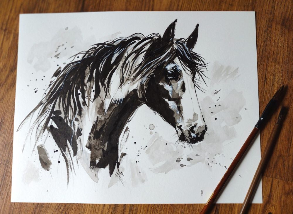 Ink wash painting of a horse head. The painting is laying on the floor with two brushes.