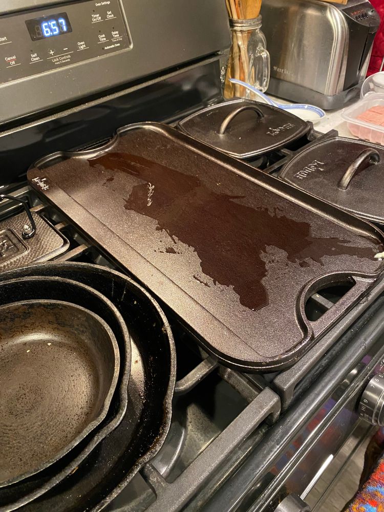 Iron griddle (about 20 inches by 8 inches) on the griddle burner of our gas stove with two iron presses next to it.  Ghee is melting on the griddle burner with.
