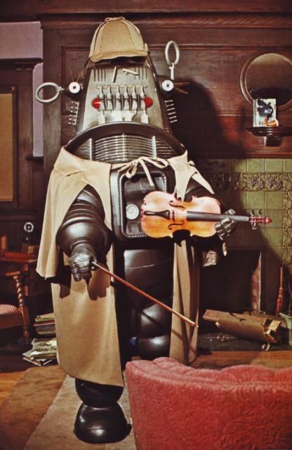 Robby the Robot from Forbidden Planet, but dressed as Sherlock Holmes, with a little Deerstalker on his dome and holding a violin, stood in an old looking Victorian study.