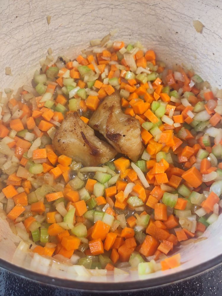 Onions, celery, carrots in a pan arranged two browned lumps of ox tail fat that will render down 