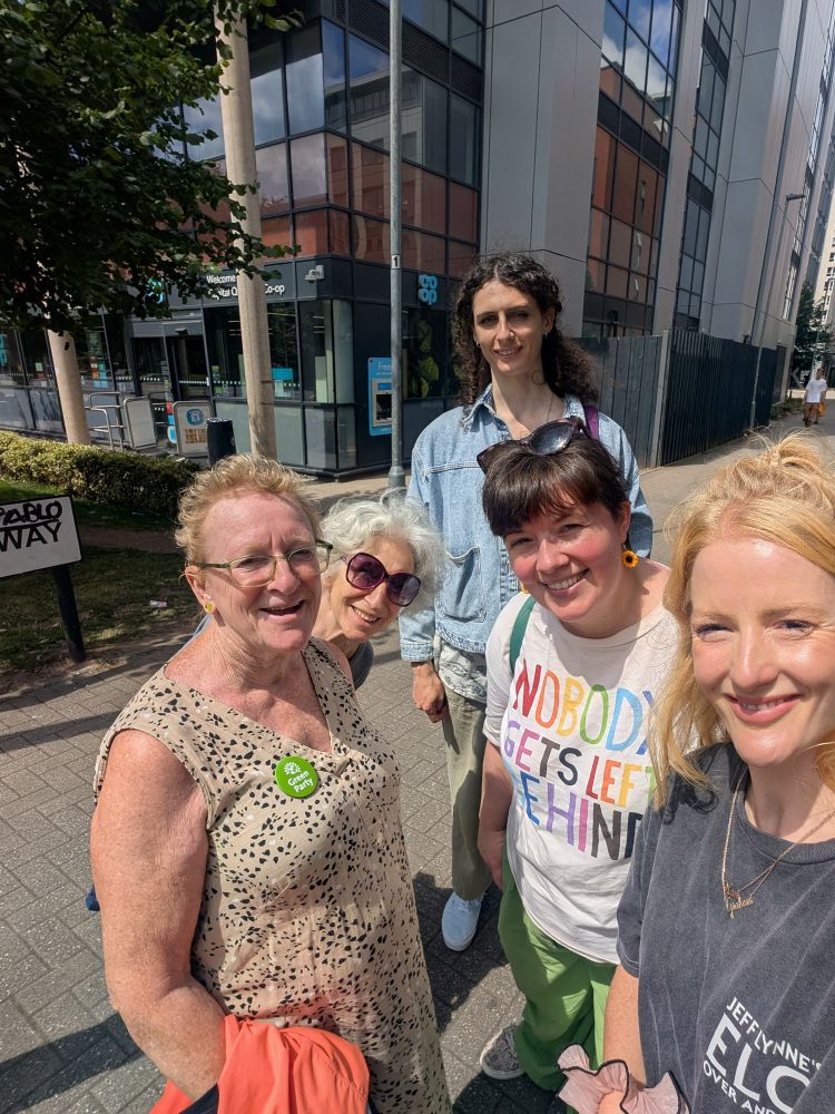 Selfie of us as a group in the sunshine, with the co op and our little Green Party office behind us.