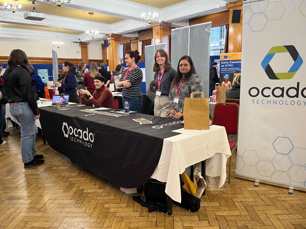 Ocado’s stall at the Lovelace Colloquium with four members of staff including Bala and Mariana, and a lot of pens. 