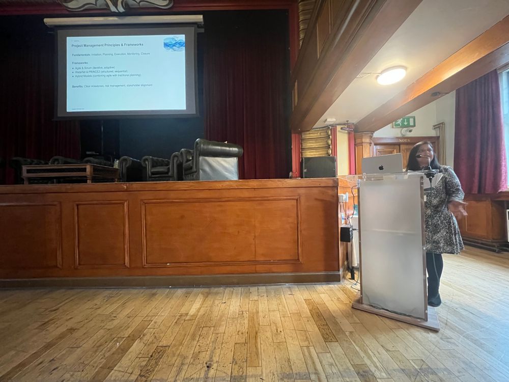 Bala Tirumalasetti speaking at the Lovelace Colloquium, with a slide describing project management principles. 