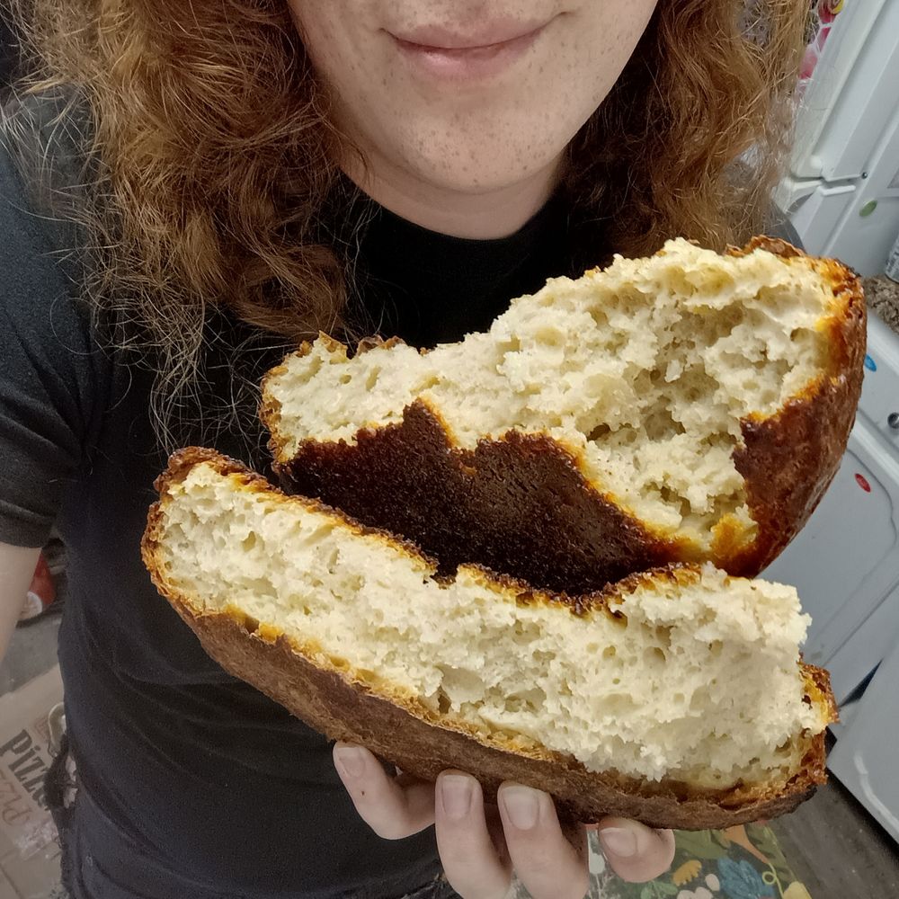 Red holding a loaf of homemade sourdough bread that's been broken in half to show off the crumb