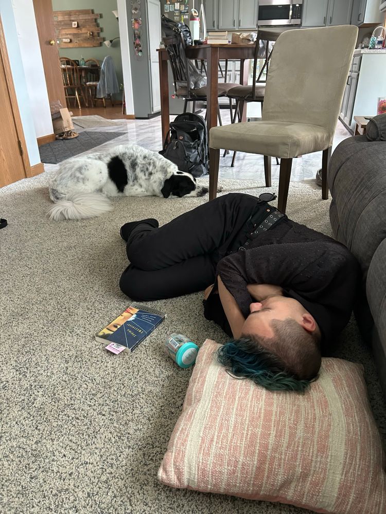 miles asleep on the ground. a container of candy and a copy of sputnik sweetheart lay next to them. oslo the black and white dog is in the background.