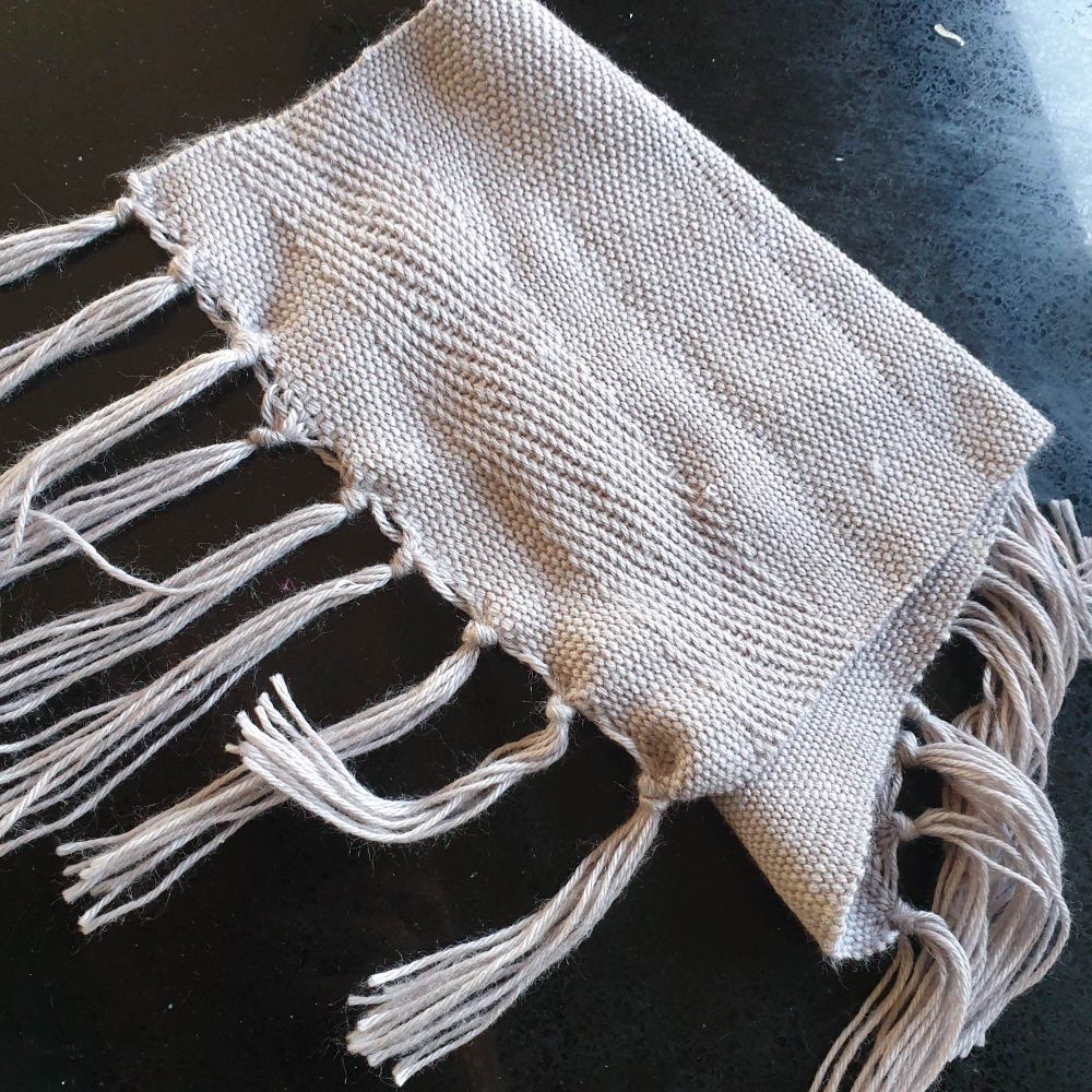 A small, folded l, grey scarf with tassels. There’s about a 1inch textured section in view in the photo. 