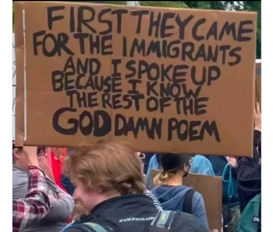Young man in a protest crowd, back to camera, holding a cardboard sign written in black marker.
"First they came for the immigrants and I spoke up because I know the rest of the goddamn poem."