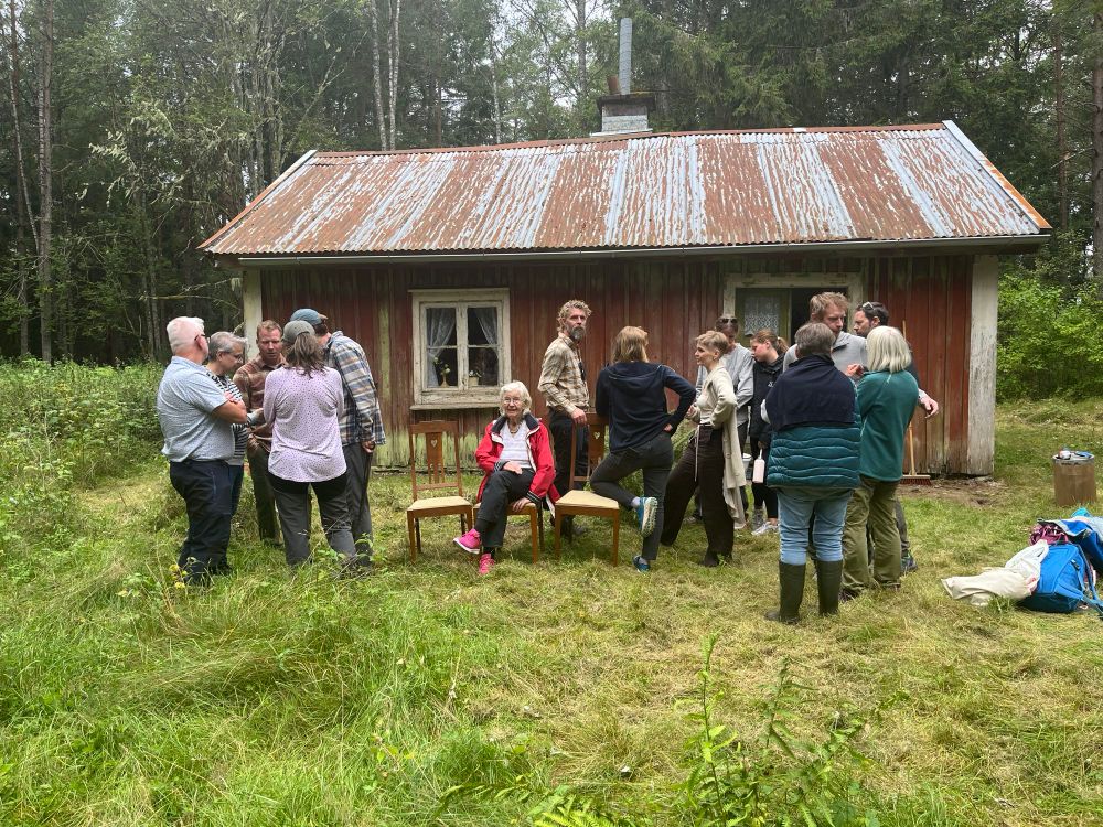 Ett 20-tal personer utanför ett litet, gammalt, lite nedgånget torp.