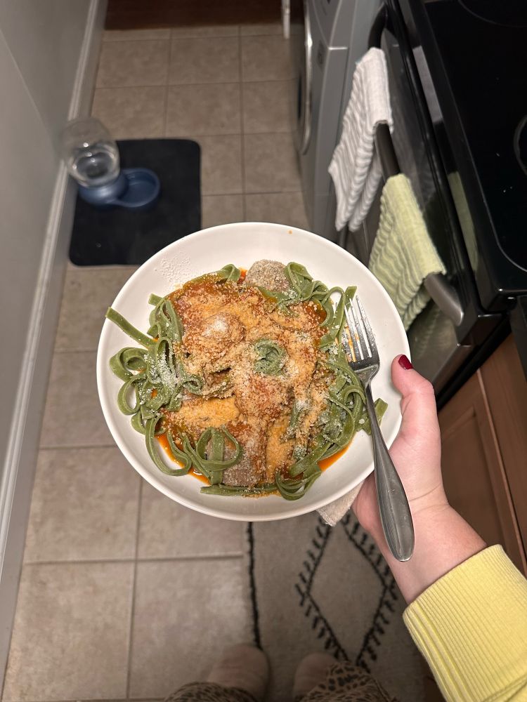 person holding a plate of green spinach fettuccini topped with turkey meatballs, tomato sauce, and grated parmesan cheese