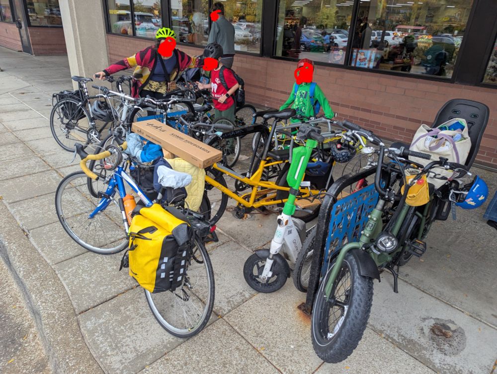 Three people holding their bikes next to completely full bike racks. There is another bike propped against the racks that are completely full.