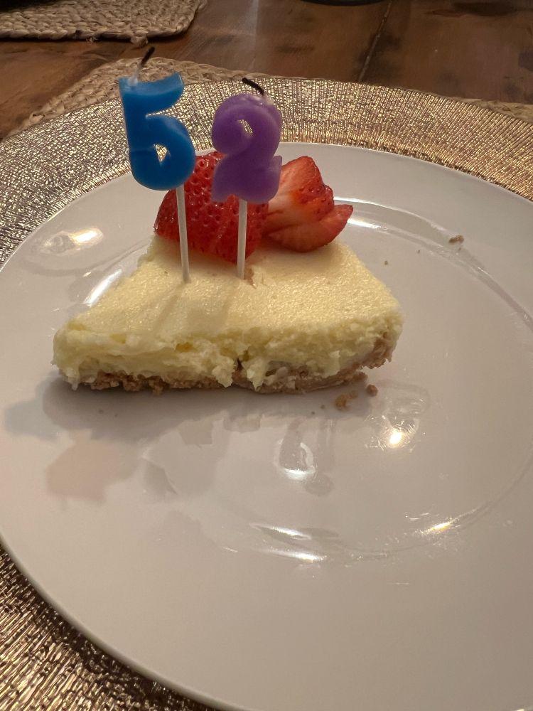 Cheesecake with strawberries, and candles with the numbers 52 on a white plate.
