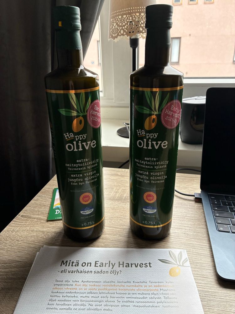 Pöydällä kaksi Happy Olive oliiviöljypulloa ja mainos missä lukee ”Mitä on varhaisen varhaisen sadon öljy”