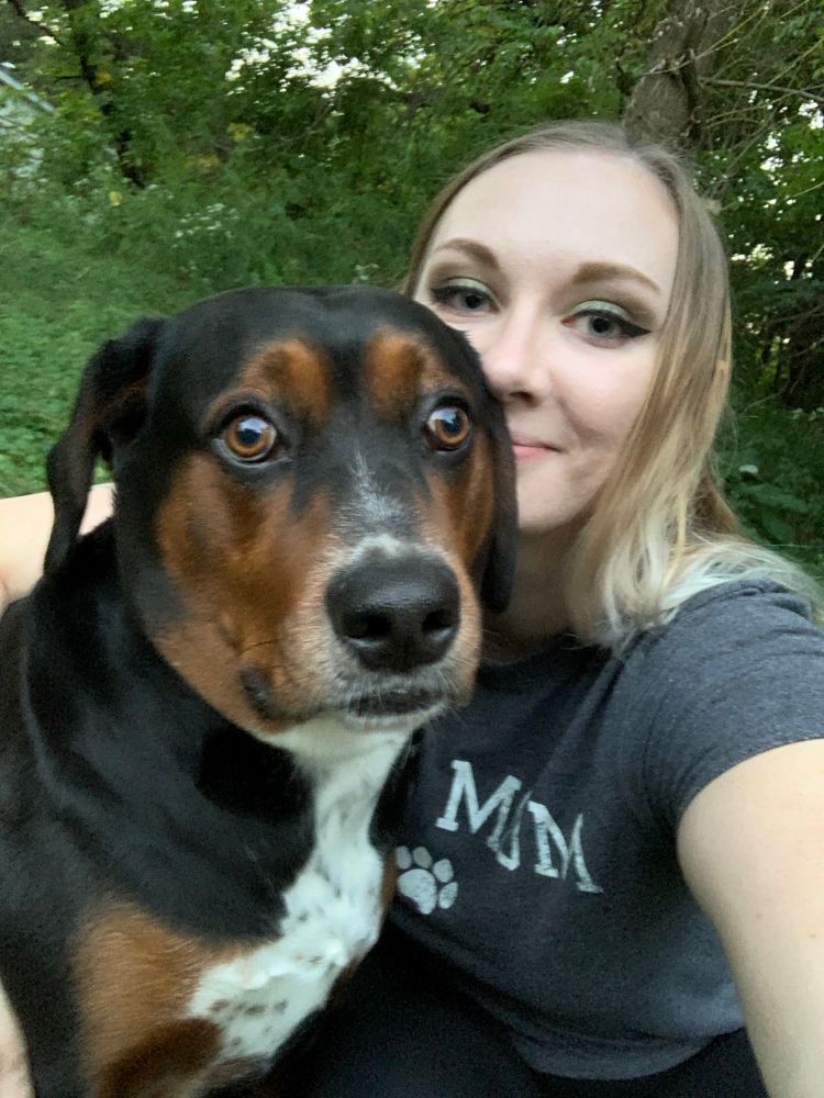 morty, a black hound dog mutt with white and tan markings, looking like he’s just witnessed something horrific. he’s camera shy and always pulls out the most ridiculous expressions when he sees my phone. hailien is smiling and attempting to pose with him. she’s wearing a “dog mom” t-shirt