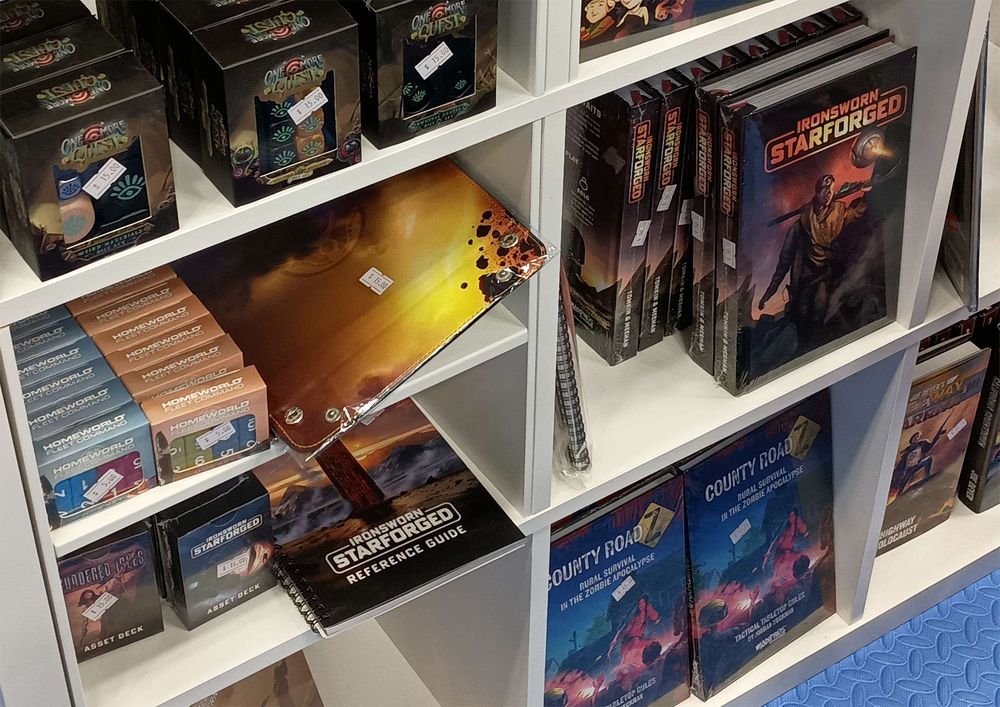 A photo of bookshelves in a trade show booth, showing Ironsworn: Starforged and Sundered Isles among other products.