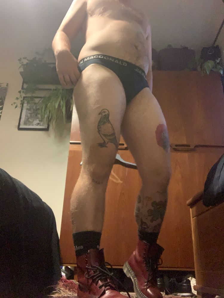 Jack stands in front of the camera (which is placed in the floor and angled slightly upwards) he is wearing only a small pair of black briefs, black socks, and loosely fastened oxblood red doc Martin’s. One hand fiddles with the waistband of his underwear. 