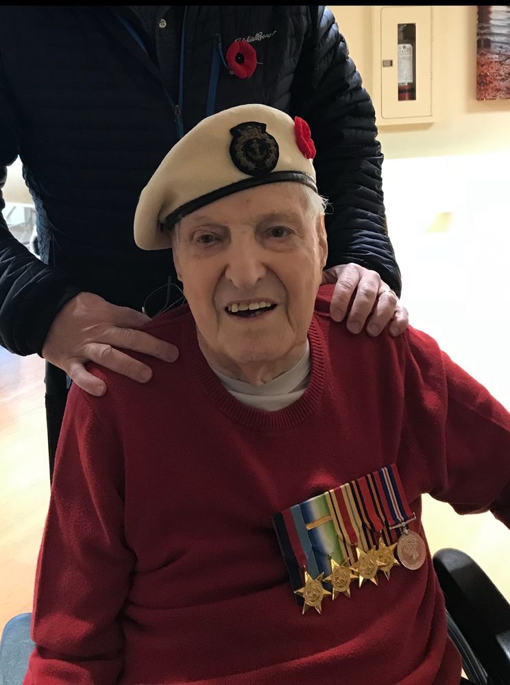 photo of a distinguished elder man in a white merchant marine cap, red sweater, and 5 medals from WWII service