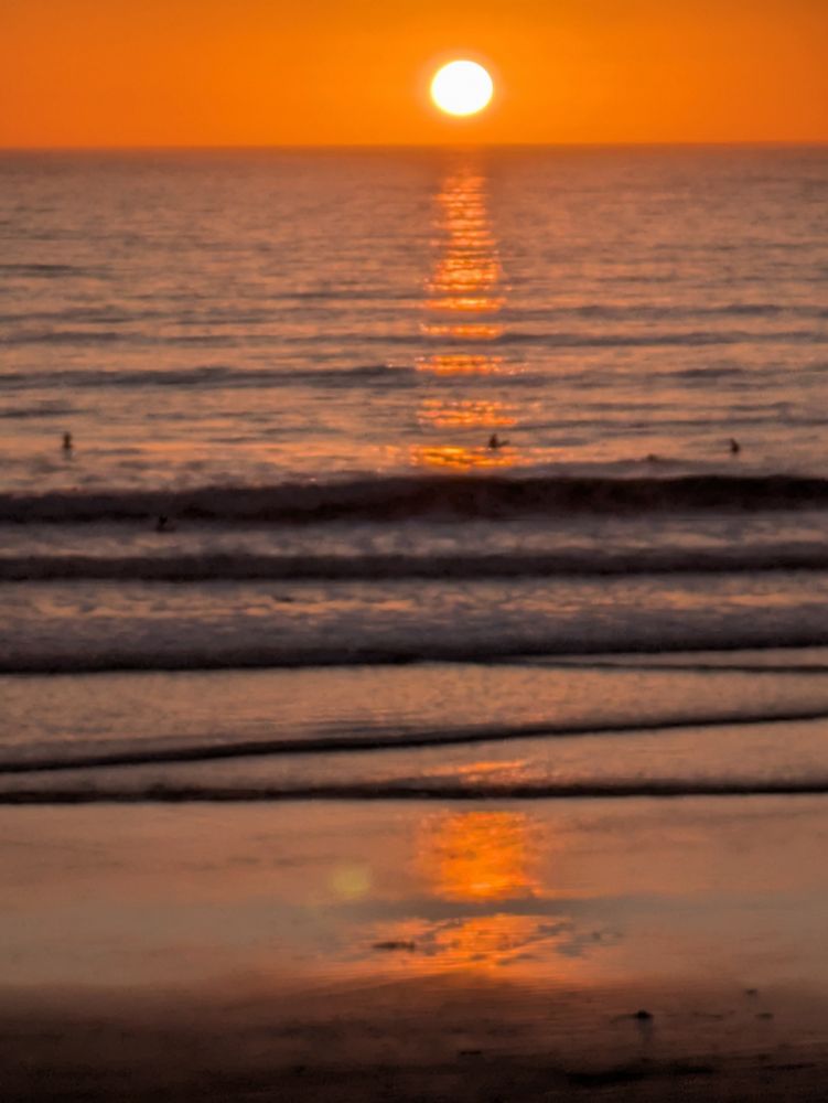 The sun just above and reflecting off the wind textured ocean horizon with nary a cloud in sight. A few surfers waiting for waves