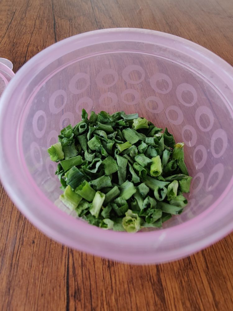 A small pink bowl with dehydrated bits of green onion in it.