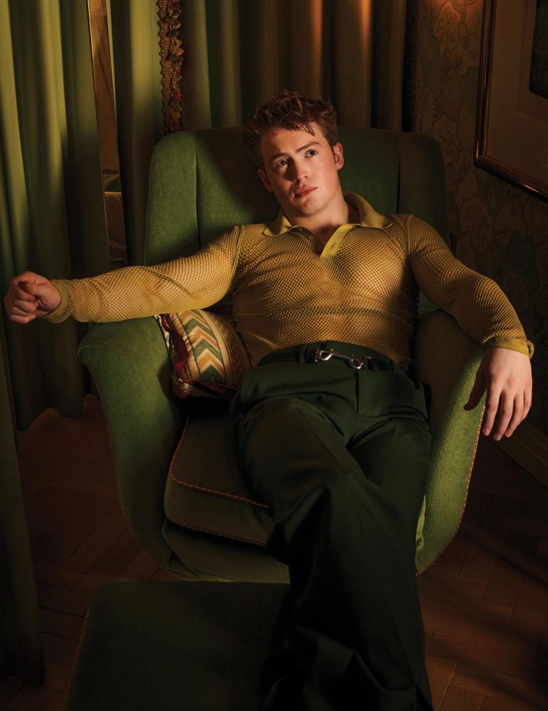 Kit Connor in a sheer yellow shirt lounging in a chair for Flaunt Magazine