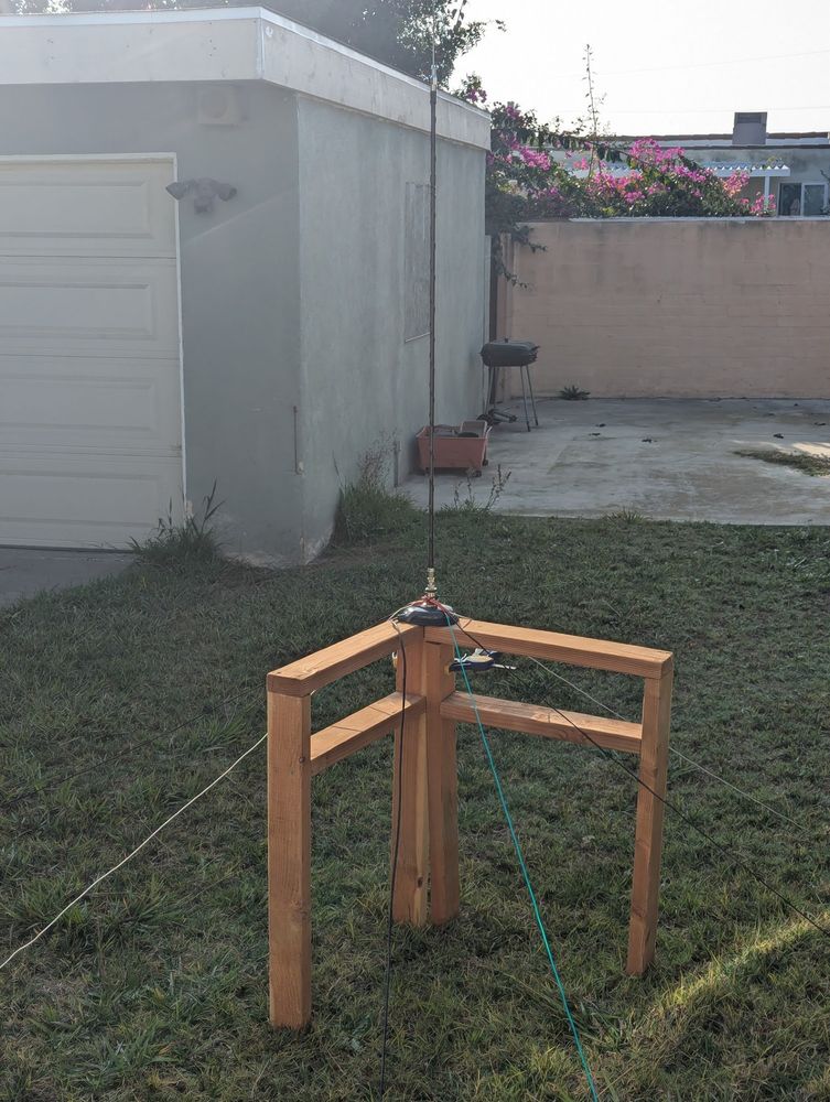 cobbled together antenna setup in my backyard. the ground radials are some extension cord snippets i had lying around, zip tied to the mobile antenna. the wood and clamps were scraps from a previous project. the antenna antenna is a 10m HamStick mobile monopole with a magnetic base