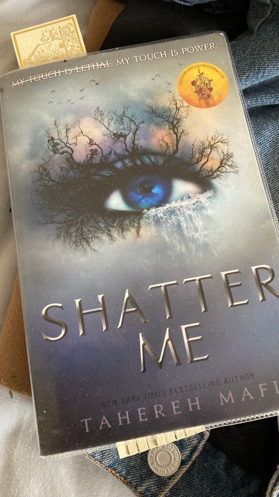 Book - Shatter Me by Tahereh Mafi. Blue cover with dystopian eye imagery with barren trees and grey sky